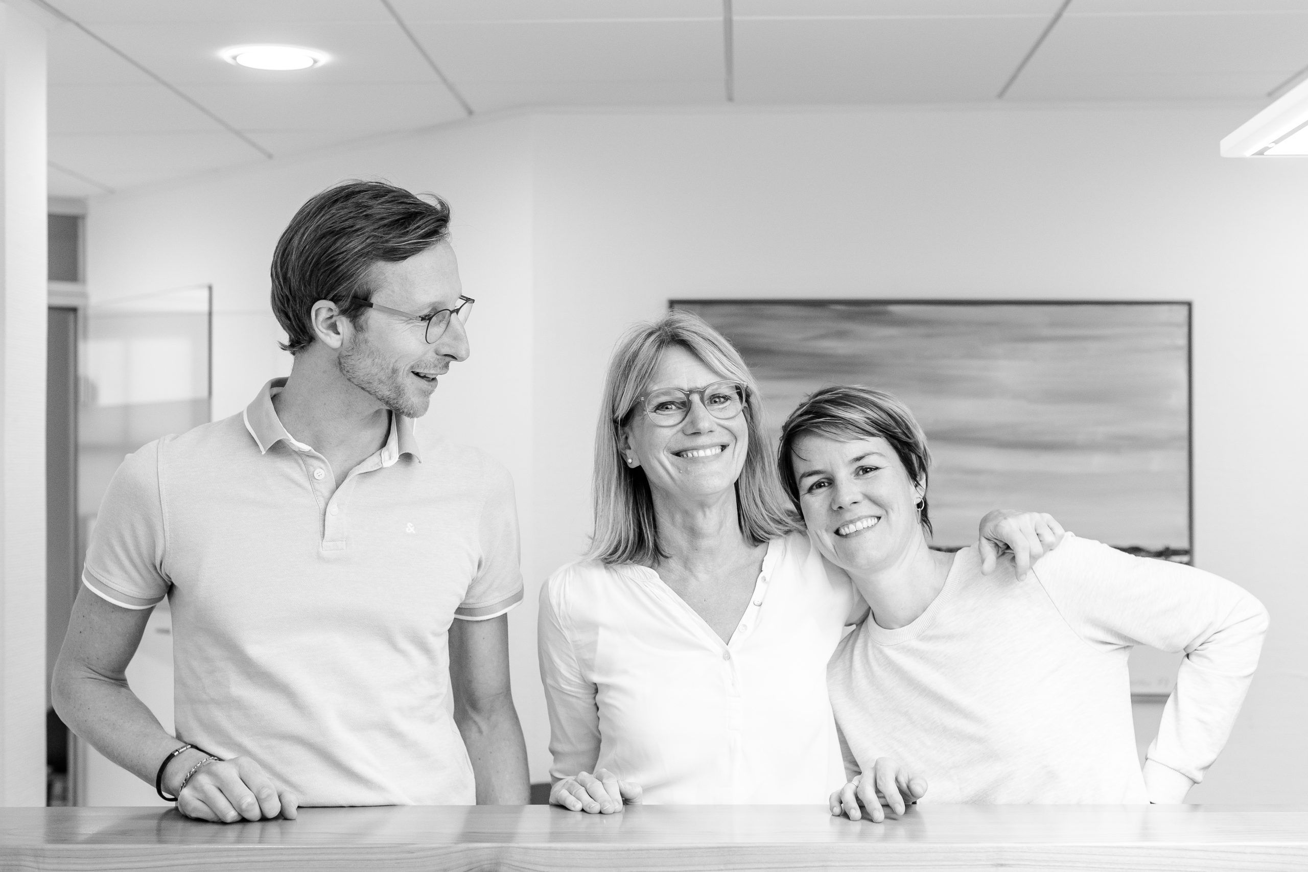 Gruppenfoto der drei freundlichen Hausärzte Dr. Uta Keller, Dr. Kristina Ott und Florian Ott, Inhaber der modernen Hausarztpraxis Dres. Keller & Ott in Garmisch-Partenkirchen, lächelnd in Praxisräumen.